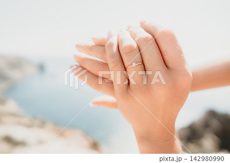 Engagement ring diamond woman hand wearing gold jewelry against a scenic bright outdoor coastline background during a sunny day 142980990