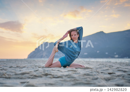 Woman practicing Eka Pada Rajakapotasana on beach during sunset Woman practicing Eka Pada Rajakapotasana on beach during sunset 142982820