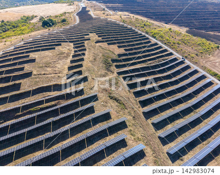 Solar panels fill dry hillside rows in large solar farm. Photovoltaic arrays stretch across landscape, creating strong geometric lines and clean energy setting under bright daylight. Solar panels fill dry hillside rows in large solar farm. Photovoltaic arrays stretch across landscape, creating strong geometric lines and clean energy setting under bright daylight. 142983074