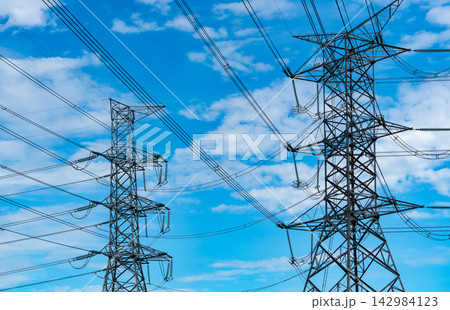 High voltage electricity transmission towers and power lines against blue cloudy sky, large scale electrical grid infrastructure supplying energy for cities, industry and modern development. 142984123