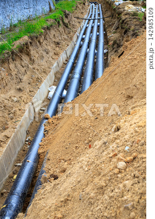 Black heating pipes in a trench. Excavated trench containing long black pipes Black heating pipes in a trench. Excavated trench containing long black pipes 142985109