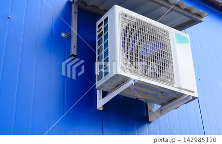 Air conditioner unit on a building wall. Outdoor air conditioning unit is mounted on a blue wall. 142985110
