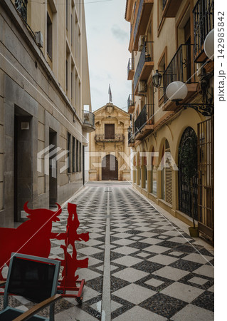 Checkerboard-tiled pedestrian alley leading to a baroque church facade in Ronda, Spain Checkerboard-tiled pedestrian alley leading to a baroque church facade in Ronda, Spain 142985842