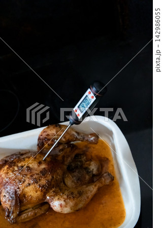 Roasted chicken with meat thermometer checking cooking temperature 142986055