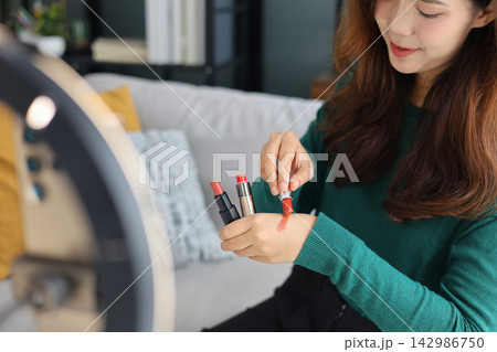 Young woman holding lipstick tubes options, beauty blogger reviewing makeup cosmetics products close up. Young woman holding lipstick tubes options, beauty blogger reviewing makeup cosmetics products close up. 142986750