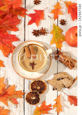 Indian masala chai with milk, ginger, anise, and cinnamon on an old wooden table with fallen autumn leaves. A traditional seasonal drink with spices, a cafe advertising card, a restaurant menu. 142987380