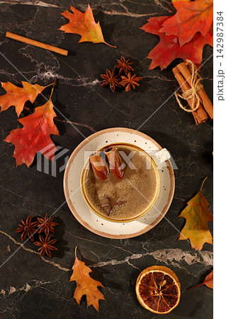 Indian masala chai with milk, ginger, anise, and cinnamon on an old wooden table with fallen autumn leaves. A traditional seasonal drink with spices, a cafe advertising card, a restaurant menu. 142987384