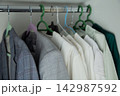 In the closet, checkered, dark and gray jackets hang on a chrome crossbar, close to a row of snow-white and light blouses on hangers. Concept: standard organization of clothes, contrast of textures 142987592