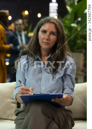 Businesswoman addresses remote colleagues during talking head videocall. Businesswoman looks toward camera while speaking to remote colleagues from rooftop lounge during teleconference meeting 142987704