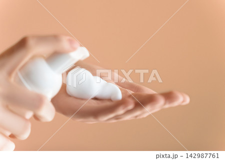 Extreme close up, female hand palm with facial foam on isolated Peach background. Young woman applying foam to washing face, beauty routine, facial cleaser. Finger presses taking foam from bottle 142987761
