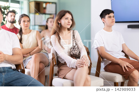 European woman is sitting among a group of people in an audience and listening to a lecture on finance 142989033