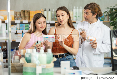 Mother and daughter choose pills in drugstore. Male pharmacist offers to buy pills Mother and daughter choose pills in drugstore. Male pharmacist offers to buy pills 142989282