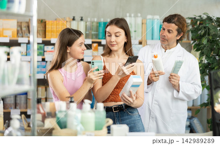 Woman with teen girl choosing and scan QR code cream at pharmacy. Man pharmacist offer European brand 142989289