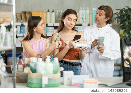 Mom and teen girl in pharmacy scans QR code ointment, pharmacist in background offer help Mom and teen girl in pharmacy scans QR code ointment, pharmacist in background offer help 142989291