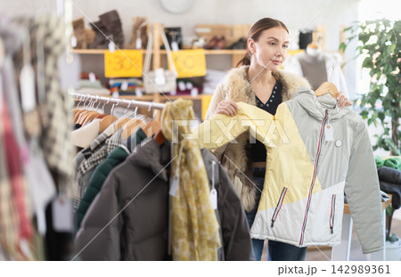 Adult woman chooses down jacket in clothing store Adult woman chooses down jacket in clothing store 142989361