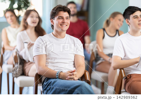 Young man listening to lecture and laughing in classroom Young man listening to lecture and laughing in classroom 142989362
