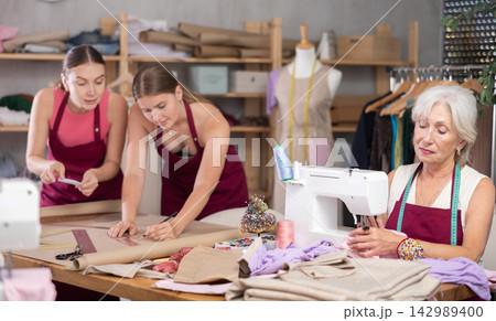 Elderly seamstress working alongside fashion designers in an atelier Elderly seamstress working alongside fashion designers in an atelier 142989400