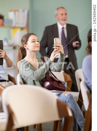 Young female student scans QR code or takes photo, teacher in background 142989402