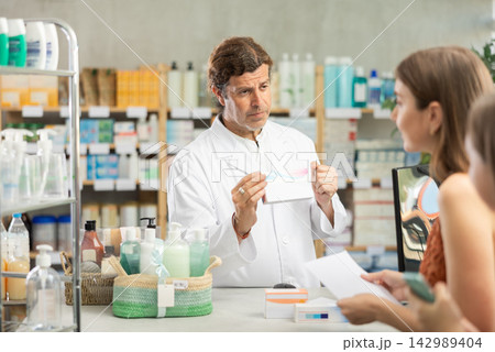 In drug store, man at counter sells medication, offer remedy to customer In drug store, man at counter sells medication, offer remedy to customer 142989404