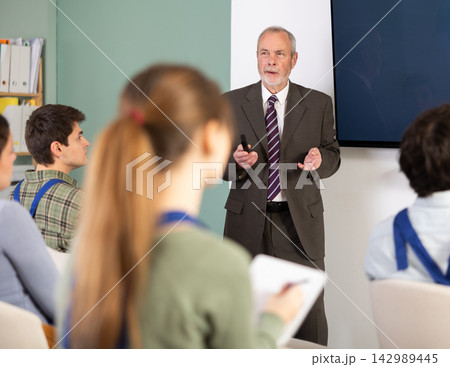 Elderly male teacher gives lecture to group of students workers Elderly male teacher gives lecture to group of students workers 142989445