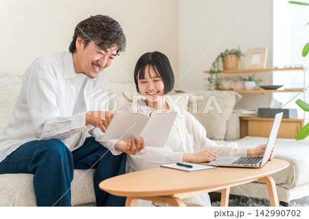 家でパパに勉強を教えてもらう高校生の女の子。教材を見ながら学習する父娘 家でパパに勉強を教えてもらう高校生の女の子。教材を見ながら学習する父娘 142990702