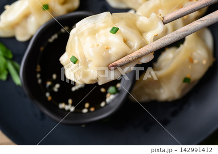 Dumpling stuffed with minced pork held by chopsticks eaten with sesame oil dipping sauce 142991412