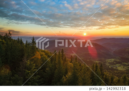 Beautiful landscape. Dramatic sunset over highland terrain. Dark pine forest illuminated with bright setting sun. Colorful nature of wild mountains Beautiful landscape. Dramatic sunset over highland terrain. Dark pine forest illuminated with bright setting sun. Colorful nature of wild mountains 142992318