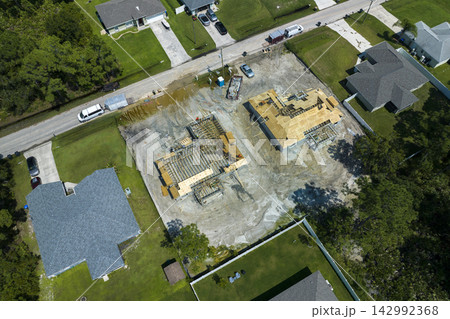 Professional builders working on roof construction of unfinished suburban home with wooden frame structure in Florida rural area. Concept of housing development in America Professional builders working on roof construction of unfinished suburban home with wooden frame structure in Florida rural area. Concept of housing development in America 142992368