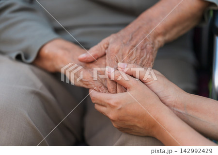 close up of senior and young holding hands on wheelchair close up of senior and young holding hands on wheelchair 142992429