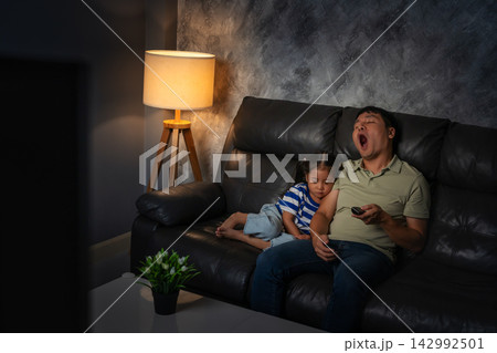 sleepy father and daughter yawning and sleeping while watching tv in the living room at night sleepy father and daughter yawning and sleeping while watching tv in the living room at night 142992501
