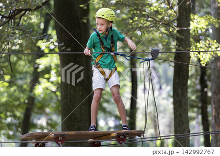 Young child boy in safety harness and helmet attached with carbine to cable on rope way in park. Young child boy in safety harness and helmet attached with carbine to cable on rope way in park. 142992767