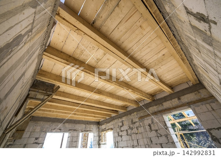 House room interior under construction and renovation. Energy saving walls of hollow foam insulation blocks, wooden ceiling beams and roof frame. House room interior under construction and renovation. Energy saving walls of hollow foam insulation blocks, wooden ceiling beams and roof frame. 142992831