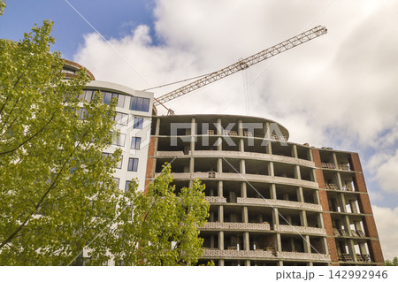Apartment or office tall building unfinished under construction among green tree tops. Tower cranes on bright blue sky copy space background. 142992946