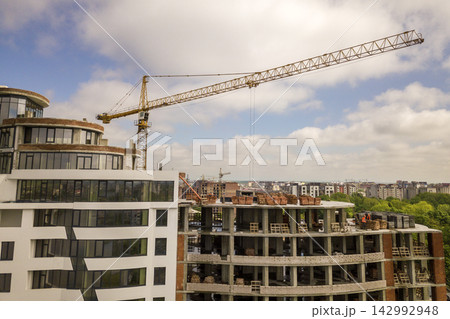 Apartment or office tall building under construction. Brick walls, glass windows, scaffolding and concrete support pillars. Tower crane on bright blue sky copy space background. 142992948