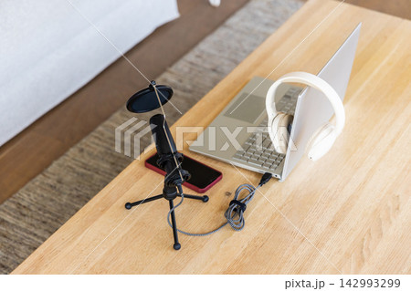 Tabletop podcasting setup showing black mic with pop filter, laptop, headphones, red phone at home 142993299