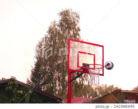 Basketball flying towards red hoop against blue sky Basketball flying towards red hoop against blue sky 142996940
