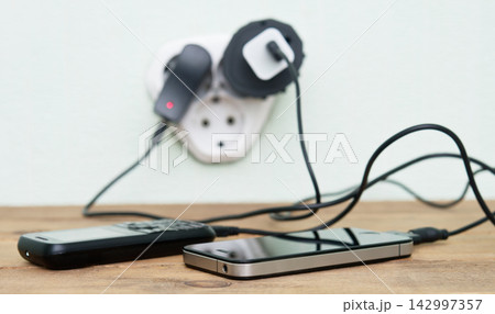 Smartphones Charging with Cables and Power Strip on Wooden Desk 142997357