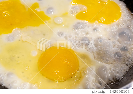 Fry eggs on pan closeup, fried cooked egg yolk and white with bubbles texture Fry eggs on pan closeup, fried cooked egg yolk and white with bubbles texture 142998102