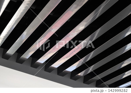 Modern interior featuring diagonal metal ceiling slats with reflective surfaces Modern interior featuring diagonal metal ceiling slats with reflective surfaces 142999282