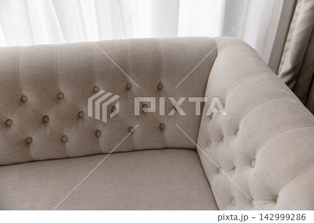 Corner of an elegant tufted beige sofa with rolled arms 142999286