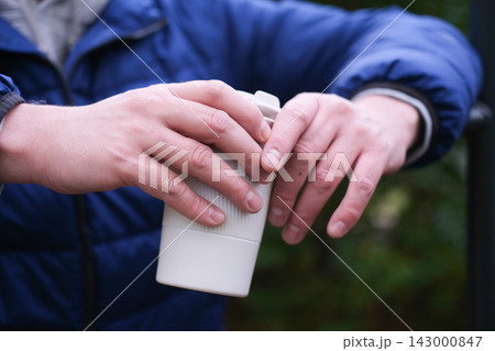 Close-up of hands holding a reusable coffee cup outdoors 143000847
