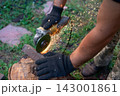 Man in protective gloves cutting metal with an angle grinder outdoors, bright sparks flying. Concept of manual labour, home workshop, DIY metalwork and work safety. 143001861