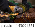 Man in protective gloves cutting metal with an angle grinder outdoors, bright sparks flying. Concept of manual labour, home workshop, DIY metalwork and work safety. 143001871