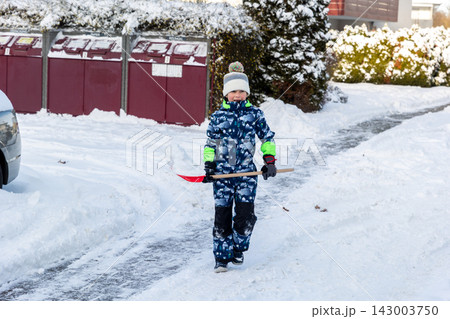 Smiling child in winter jumpsuit holds red shovel with snow on residential street in Magdeburg. Sunny neighborhood scene shows outdoor play, snow removal, and family life beside parked cars Smiling child in winter jumpsuit holds red shovel with snow on residential street in Magdeburg. Sunny neighborhood scene shows outdoor play, snow removal, and family life beside parked cars 143003750