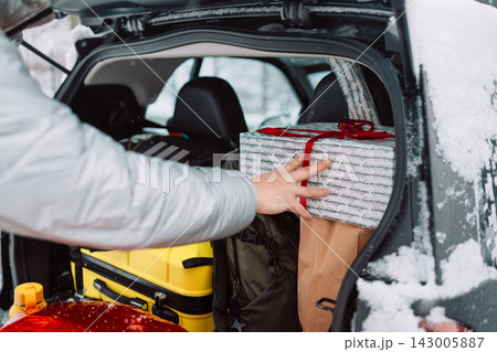 Man loading luggage and gift box into car trunk in winter 143005887