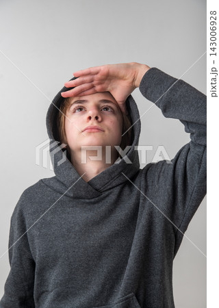 Young person wearing a grey hoodie looking up, hand shading eyes, thoughtfully searching for new ideas, opportunities, and future possibilities with curiosity Young person wearing a grey hoodie looking up, hand shading eyes, thoughtfully searching for new ideas, opportunities, and future possibilities with curiosity 143006928