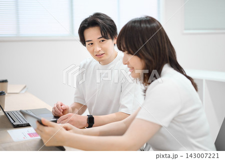 タブレットで作業をする若い女性と同僚の男性 タブレットで作業をする若い女性と同僚の男性 143007221