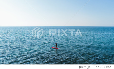 Young person paddleboarding on endless blue ocean Young person paddleboarding on endless blue ocean 143007562