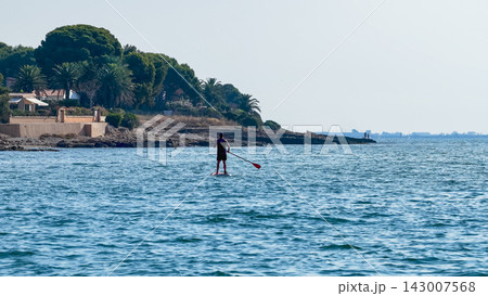 Man paddleboarding along Mediterranean coast on sunny day Man paddleboarding along Mediterranean coast on sunny day 143007568