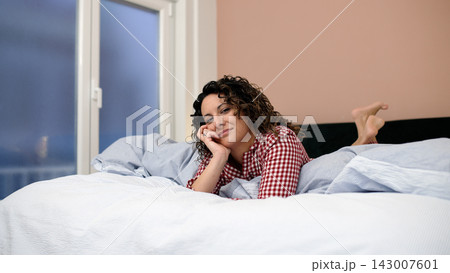 Woman relaxing in bed at home looking at camera 143007601